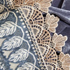 Close-up of a dark gray quilted fabric with beige lace trim and white embroidered floral patterns.