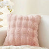 A fluffy, light pink faux fur throw pillow resting on a white surface next to a white plant.