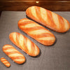 A loaf of French bread shaped like a pillow, featuring striped golden-brown crusts, resting on a dark gray fabric.