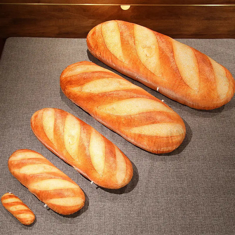 A loaf of French bread shaped like a pillow, featuring striped golden-brown crusts, resting on a dark gray fabric.