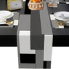 A modern geometric placemat set featuring black, gray, and silver patterns with natural wood accents on a dining table.