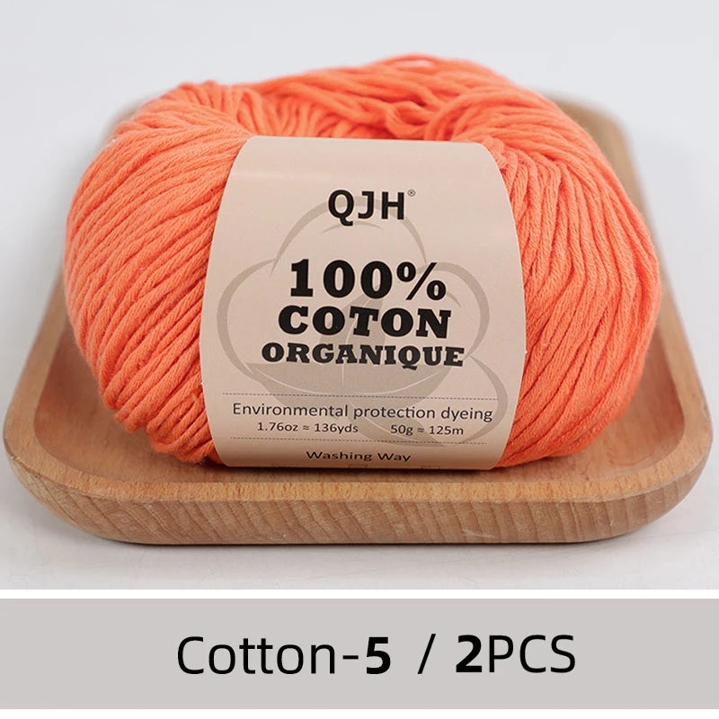 A ball of bright orange 100% organic cotton yarn labeled QJH for knitting and crochet