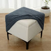 A navy blue geometric jacquard ottoman slipcover draped over a white upholstered ottoman.