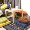 A collection of tufted corduroy floor seat cushions in yellow, blue, green, and brown resting on a patterned rug.