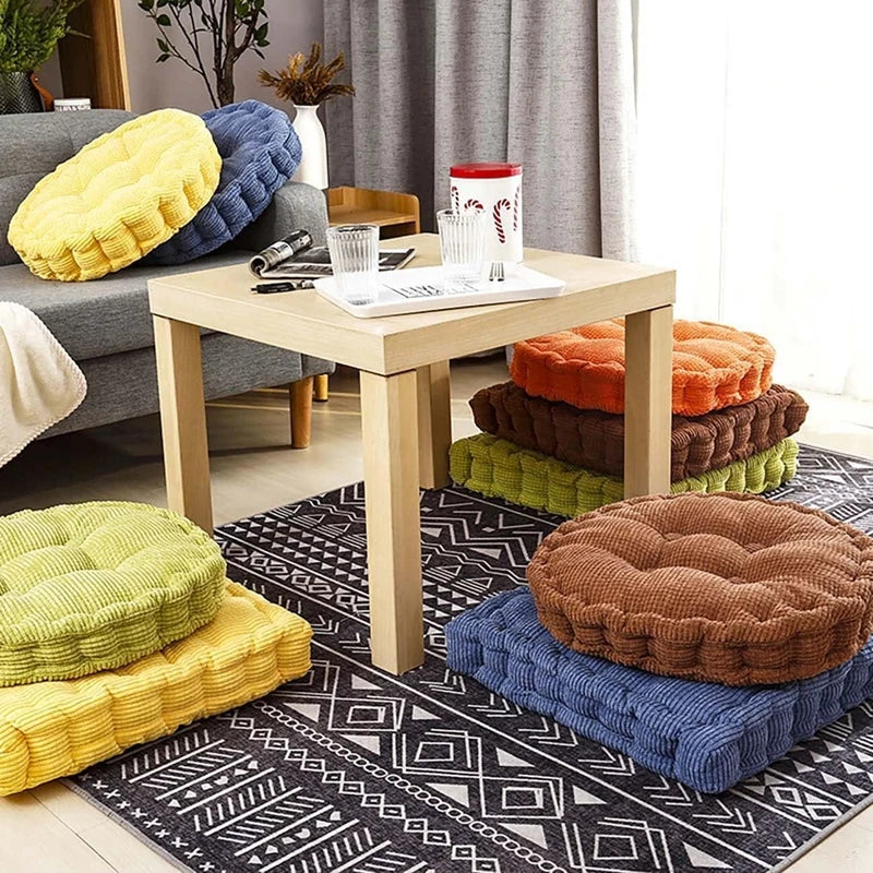 A collection of tufted corduroy floor seat cushions in yellow, blue, green, and brown resting on a patterned rug.