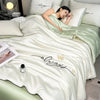 A white ultra-soft ice silk fiber summer quilt draped over a bed, featuring elegant script embroidery.
