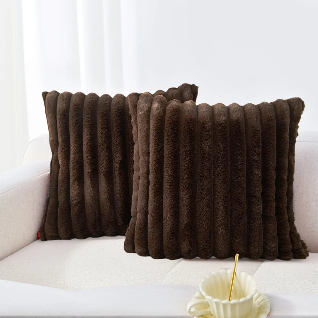 A set of two dark brown plush, vertically striped decorative pillowcases resting on a white sofa.