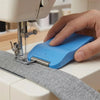 A hand is using a blue magnetic seam guide with a stitch gauge on a sewing machine.