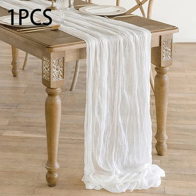A white semi-sheer gauze table runner draped over a wooden dining table.