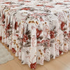 A white floral ruffle bed skirt set featuring red and green botanical patterns on a wooden floor.