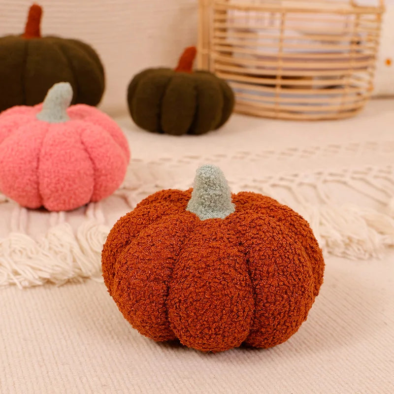 A textured, orange 3D pumpkin shaped throw pillow with a green stem resting on a light beige fabric.