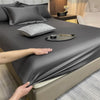 A dark gray fitted bed sheet is draped over a bed, with pillows and decorative items visible.
