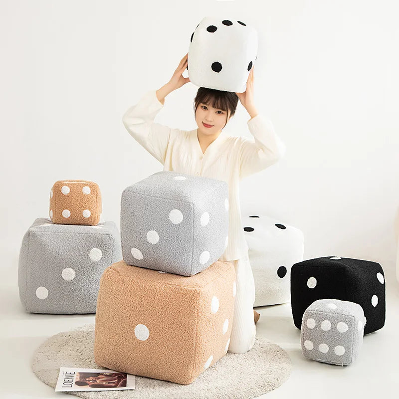 A person holds up a white plush dice cube cushion with black polka dots against a white background.