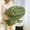 A hand holds a large, textured, olive green plush winter blanket against a white background.