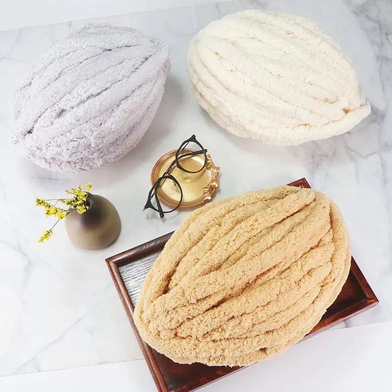 Three balls of extra thick hand-knitted yarn in white and beige tones displayed on a marble surface.