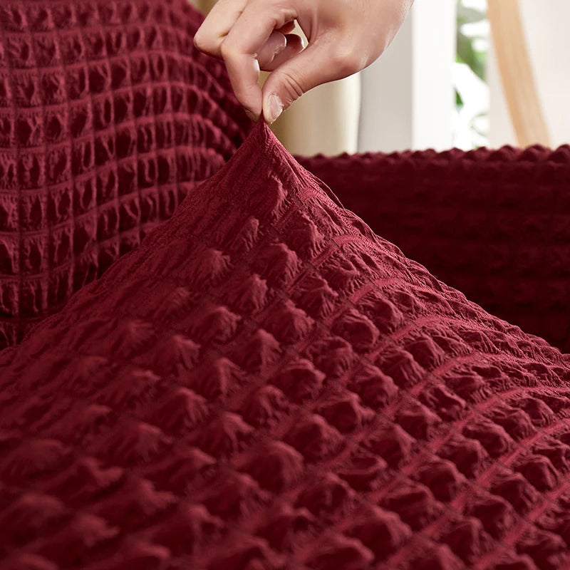 A hand is touching the textured, deep red stretch knit sofa cover with a bubble lattice pattern.