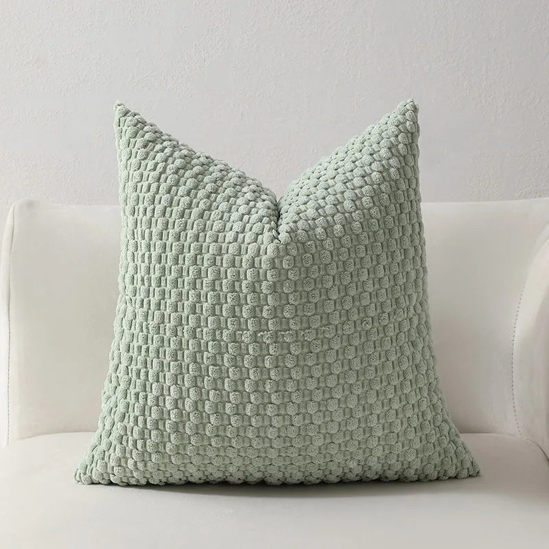 A light sage green textured decorative pillow with a ruffled edge and zipper closure.
