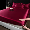 A deep burgundy satin fitted sheet is laid out on a bed, with a hand touching the fabric.