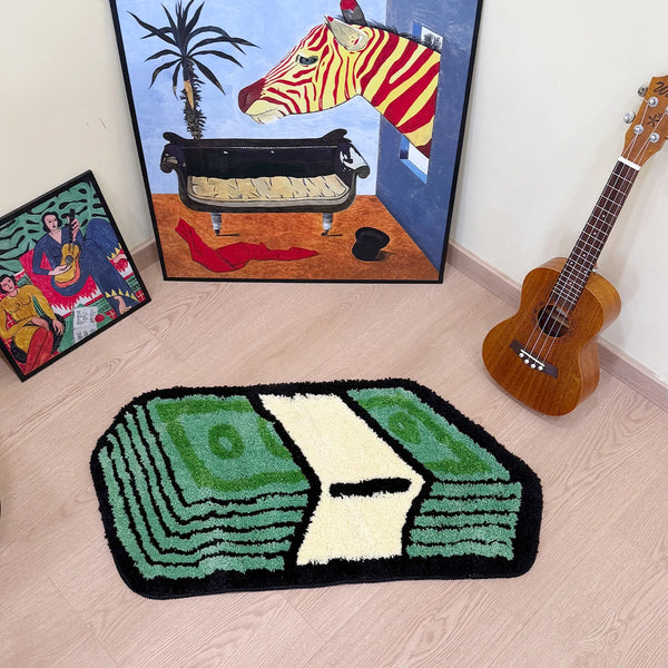A green and black tufted bathroom rug is placed on a light wood floor in front of a framed cartoon painting.