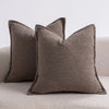 Two solid brown textured boucle throw pillows resting on a light-colored surface.