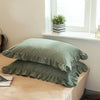 A set of two soft plaid washed cotton pillowcases with ruffled edges resting on a light-colored surface.