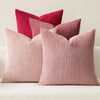A set of four textured throw pillows in shades of pink and coral are displayed on a white sofa.