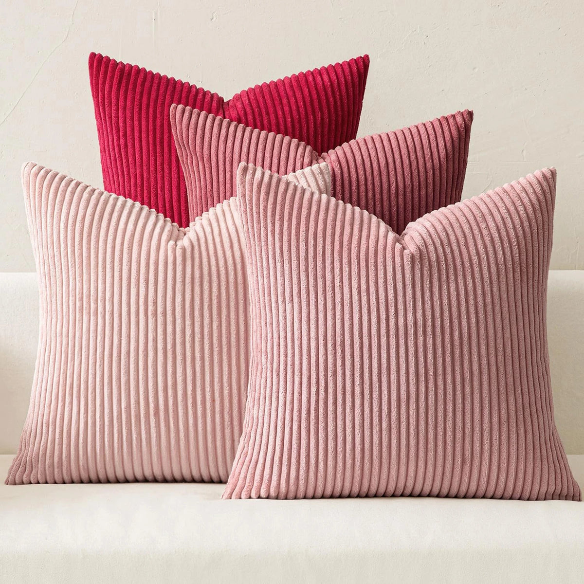 A set of four textured throw pillows in shades of pink and coral are displayed on a white sofa.