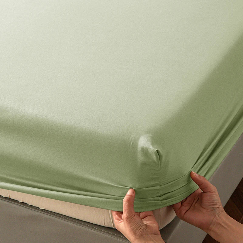 A hand is holding up a light green soft touch microfiber fitted sheet to show its deep pockets.