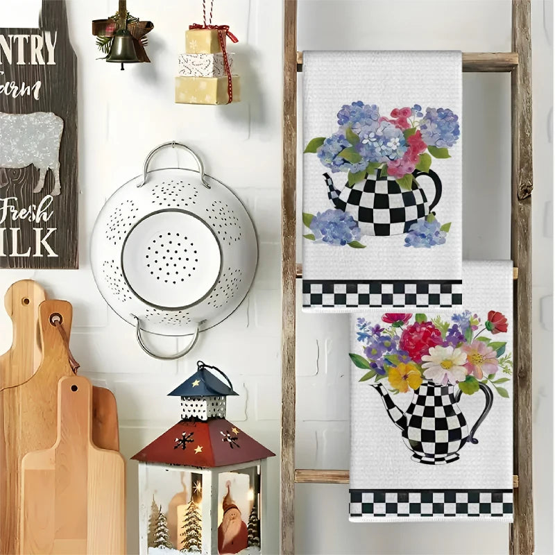 A set of two black and white checkered kitchen towels featuring a floral teapot design hanging on a wooden rack.