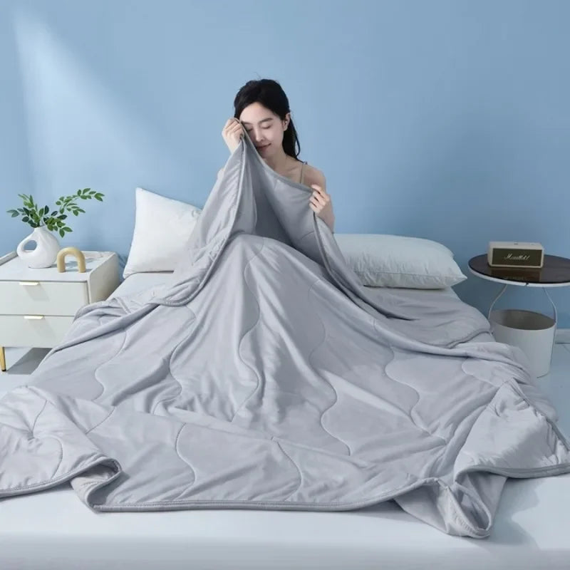 A gray Summer Wave Grid Quilt is draped over a bed, with a person resting their head on the fabric.