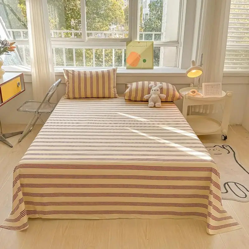 A bed dressed with striped organic cotton bedding, featuring a flat sheet and pillows, next to a window.