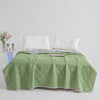 A light green quilted blanket is spread on a bed with white pillows.