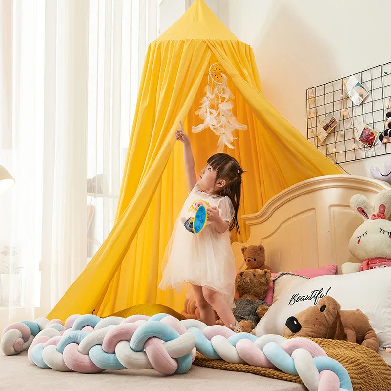 A young girl stands inside a yellow princess hanging bed canopy with a light-colored dress.