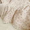 A soft, light pink floral print muslin blanket is folded and draped on a white surface.