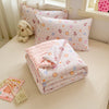 A pink and white quilted blanket with a floral pattern is displayed on a light-colored surface next to a stuffed animal.
