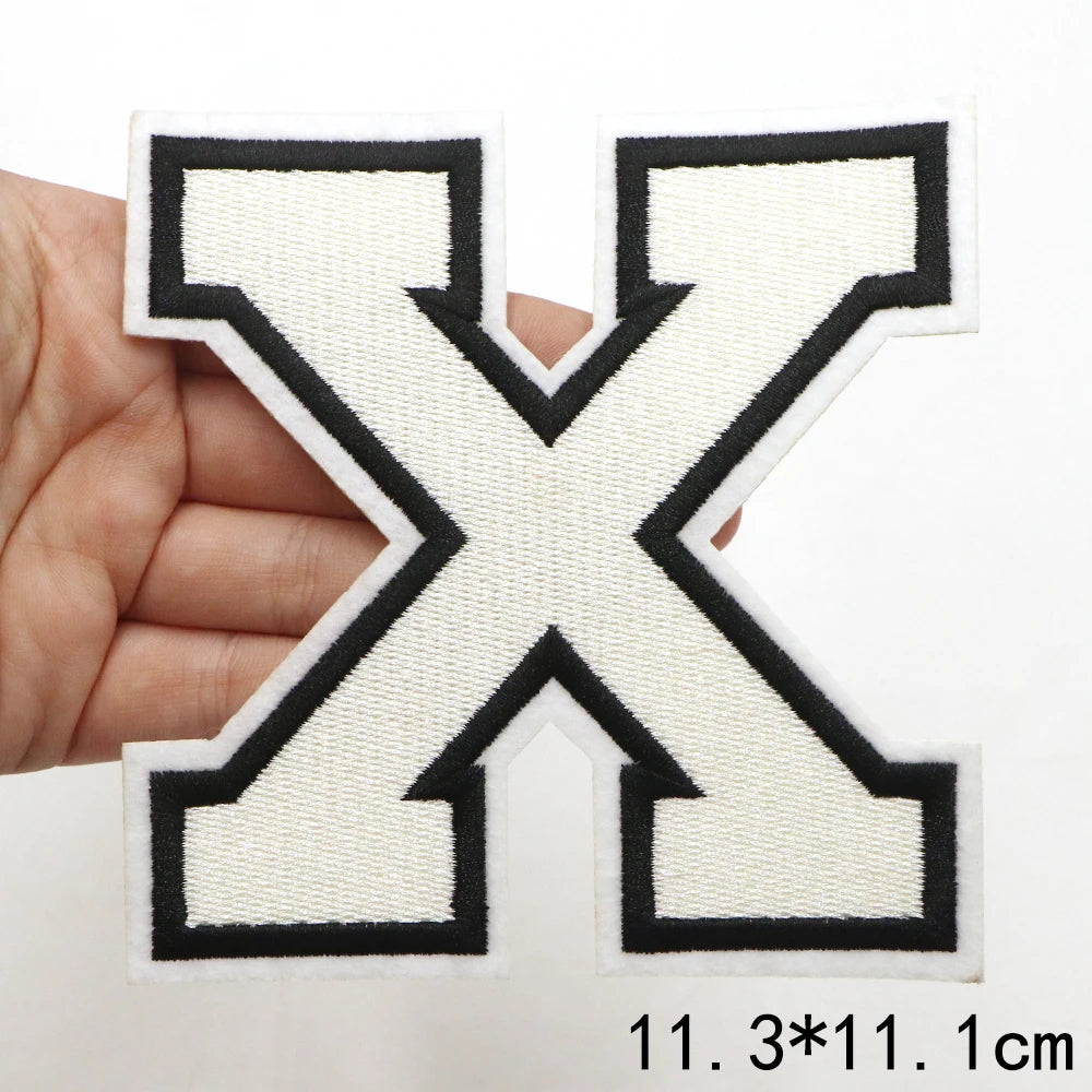 A hand holds a large black and cream letter X patch for clothing decoration.