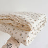 A stack of cream-colored muslin blankets with a delicate floral print, folded on a white surface.