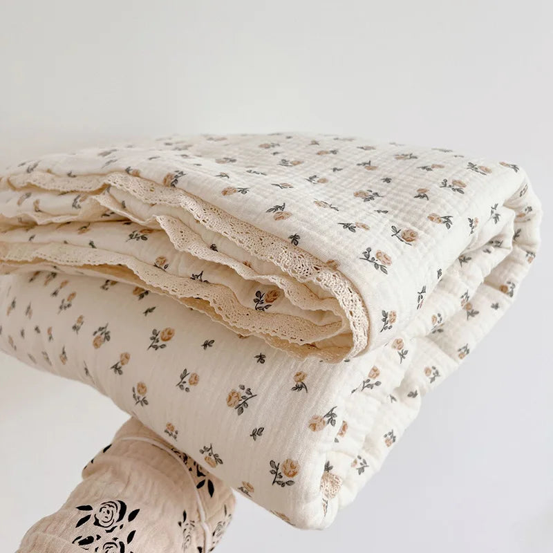 A stack of cream-colored muslin blankets with a delicate floral print, folded on a white surface.