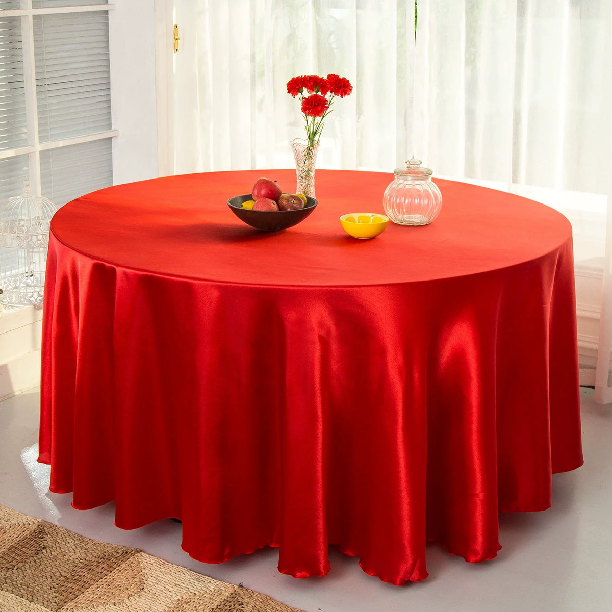 A round table set with a red satin cloth, featuring fruit and a glass vase on a white table.
