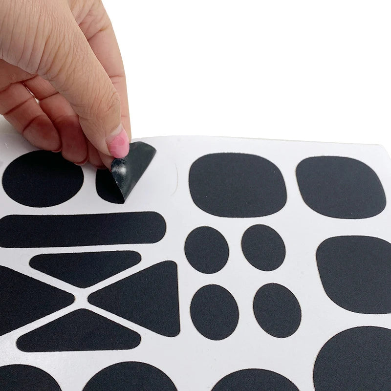A hand is applying a black self-adhesive fabric repair patch onto a white surface with various shapes of patches visible.