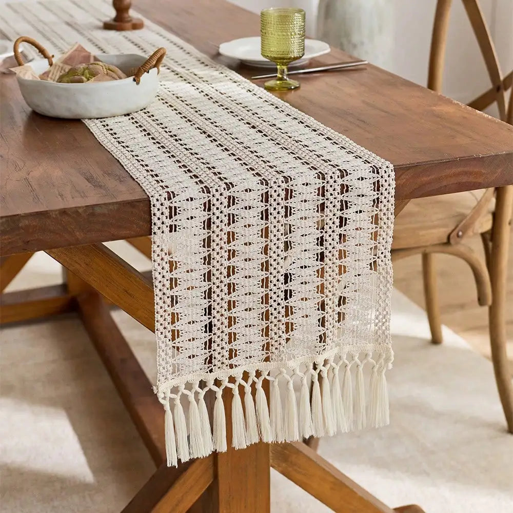 A cream macrame table runner with fringe is displayed on a wooden dining table.