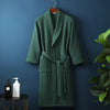 A dark green cotton terry robe hanging on a wall, displayed next to some skincare products.