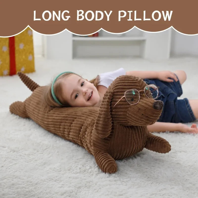 A young girl is lying on a white rug with a brown corduroy sausage dog body pillow and clear glasses.