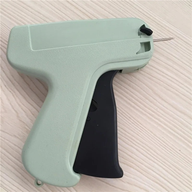 A light green precision sewing tag gun with a black handle and a metal needle visible.