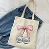 A beige canvas shopping bag featuring a pink bow tied around a pair of silver, spherical earrings.