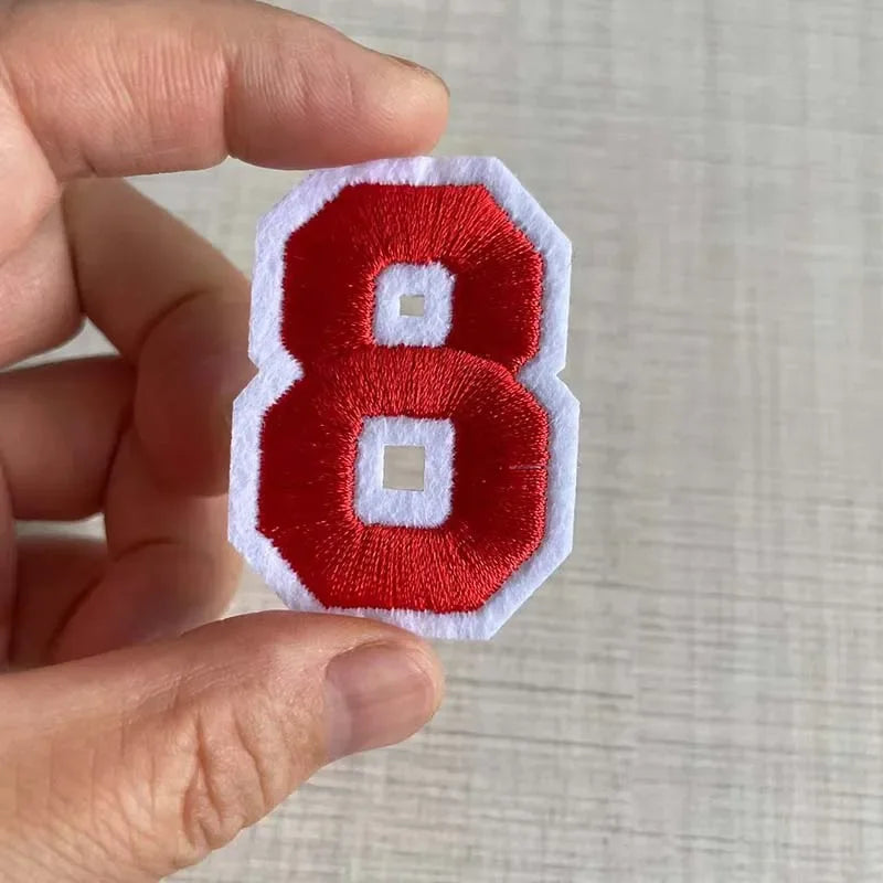 A hand holds a red and white embroidered number 8 patch for apparel.