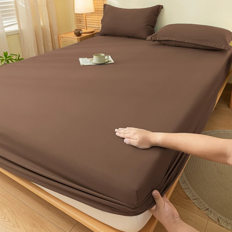 A close-up of a brown fitted bed sheet set on a bed, with a hand adjusting the fabric.