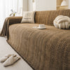 A brown textured sofa cover featuring an elegant fishbone pattern, with a white mug and knitted accessories nearby.