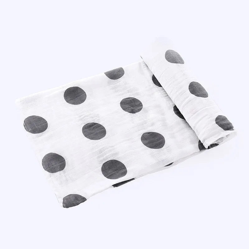 A white muslin swaddle blanket with small gray polka dots folded and displayed on a white background.