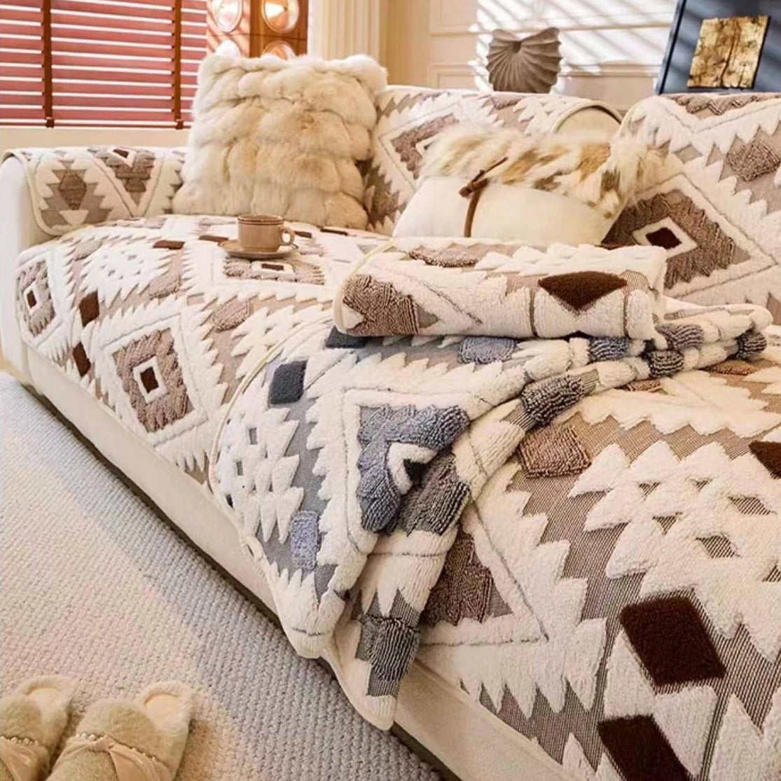 A beige and brown patterned fleece sofa slipcover with faux fur pillows and a matching blanket.